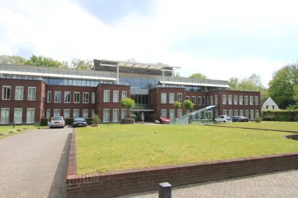 Modern kantoorgebouw aan de Arnhemse Bovenweg met glazen entree, rode bakstenen gevel en geparkeerde auto's op de oprijlaan.
